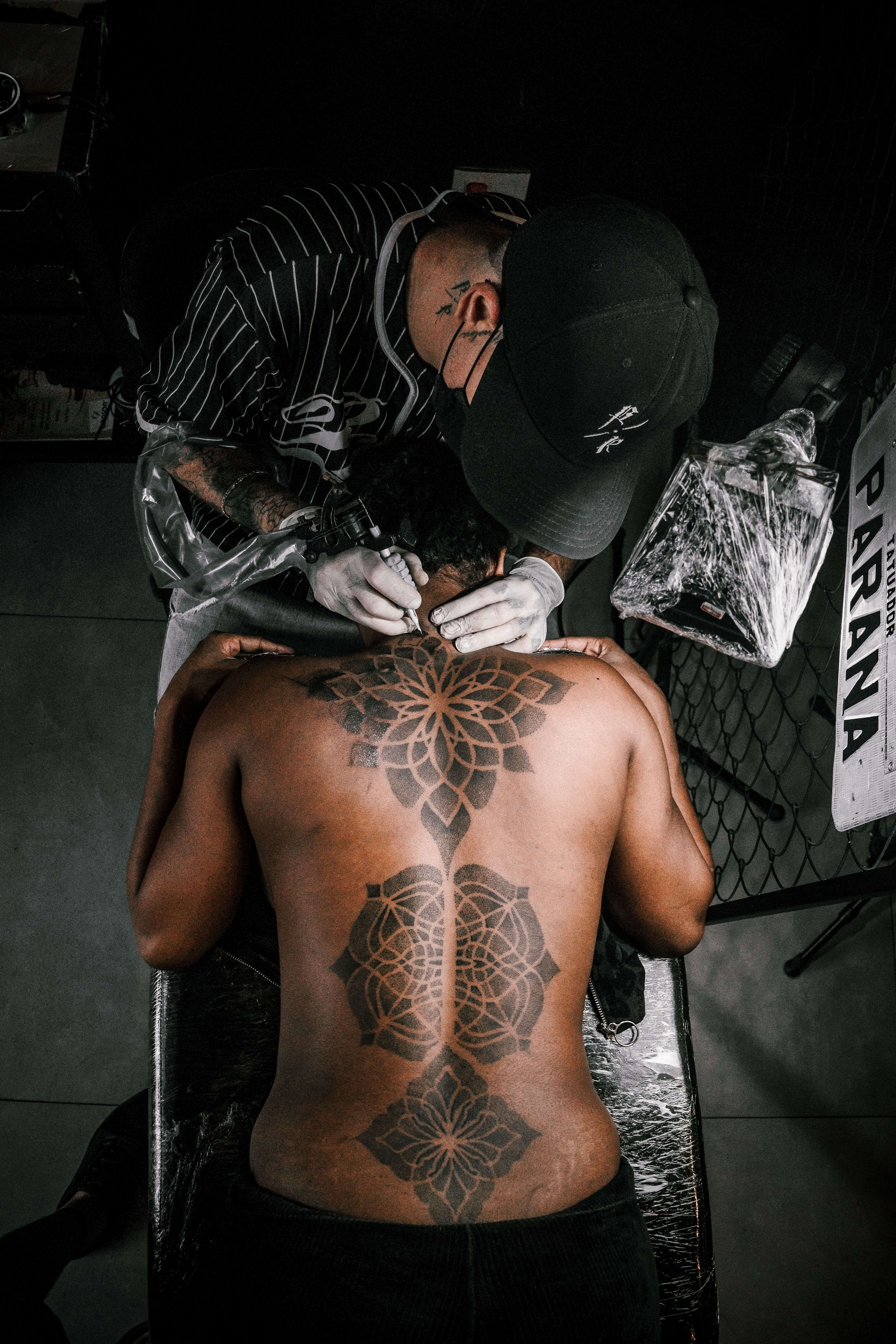 Tatuador aplicando mandala nas costas de cliente masculino